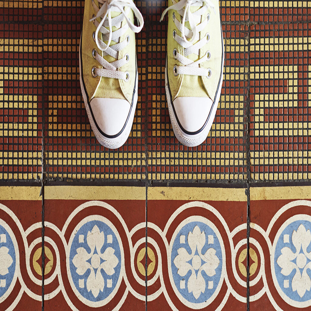 Unique home remodeling ideas. This image shows a woman standing ona. mosaic inlay rug with a tile border in her home. The purpose is to inspire creative uses of tile rugs in homes.