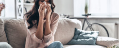 Remodeling tips for removing allergens from home during allergy-season. Sick young woman blowing the nose using tissue paper while sitting on the sofa at home