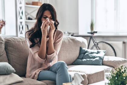 Remodeling tips for removing allergens from home during allergy-season. Sick young woman blowing the nose using tissue paper while sitting on the sofa at home